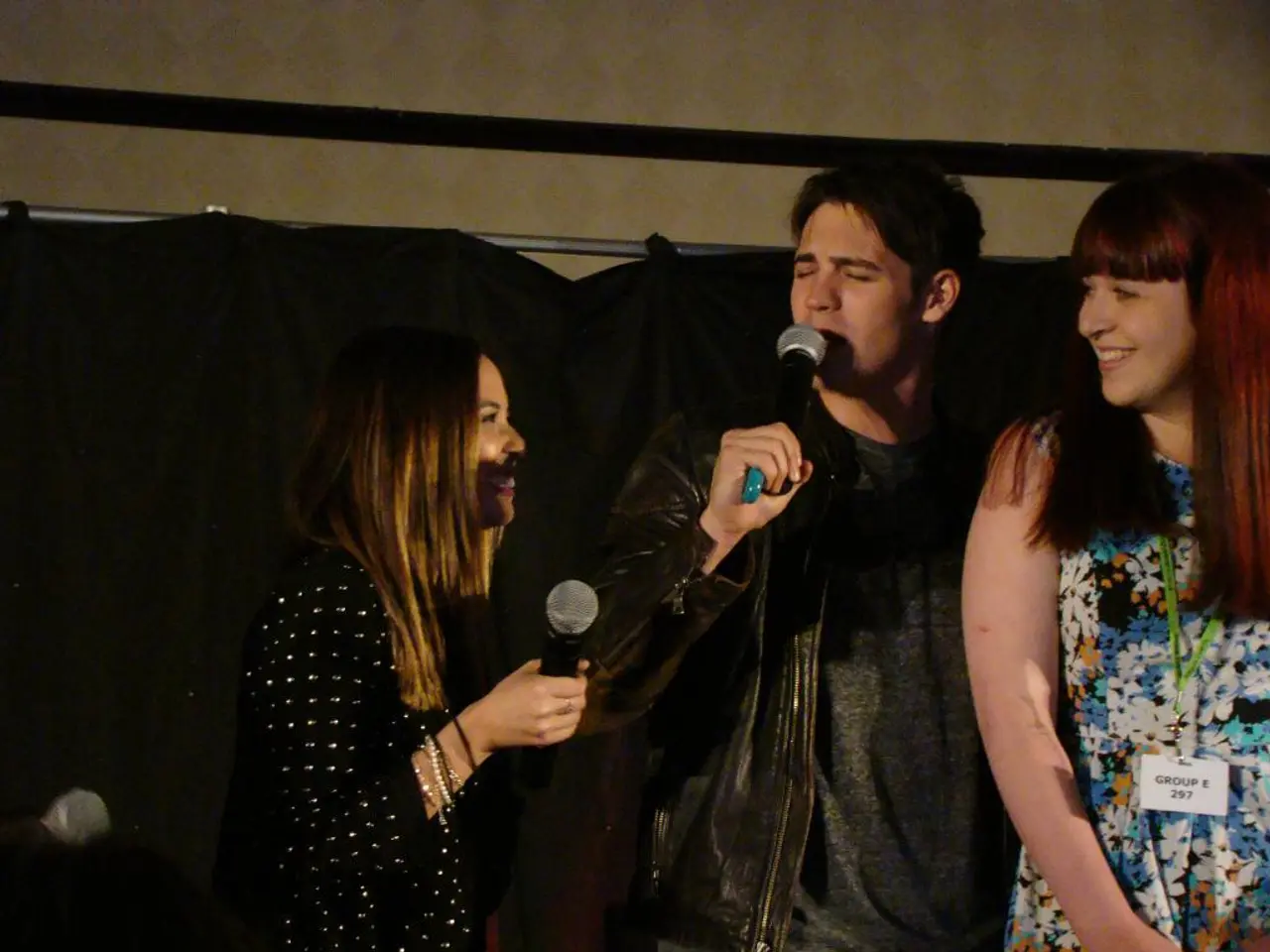 This picture shows three people standing and two people speaking with the help of a microphone
