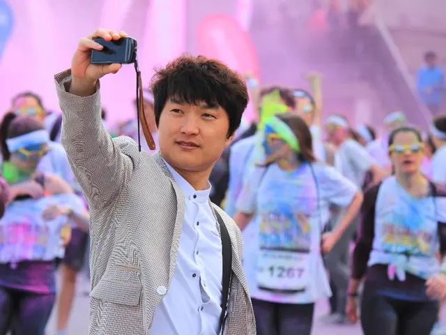 There is a person holding mobile. In the back there are many people. Some are wearing goggles,...